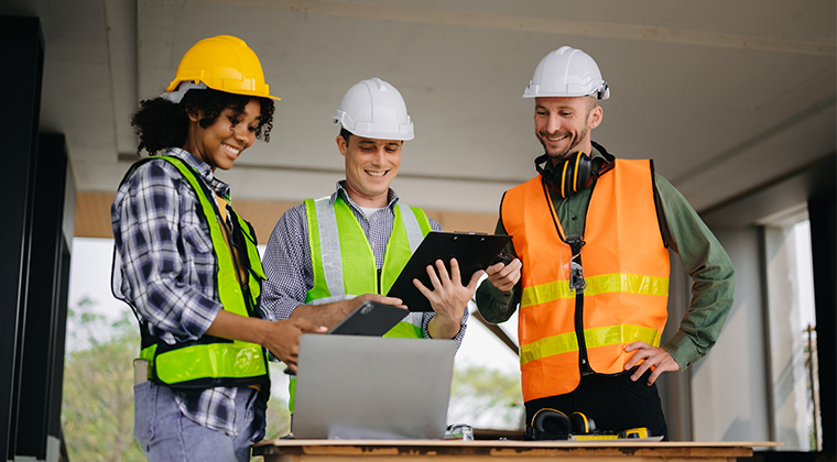 Smiling construction workers review data on a laptop
