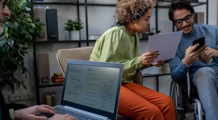 two people talking with a laptop in the foreground